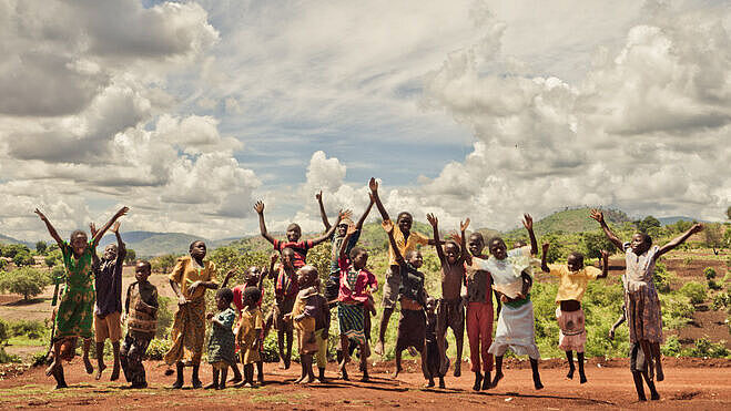 Eine Gruppe afrikanischer Kinder springt in die Luft und streckt die Hände gegen den Himmel