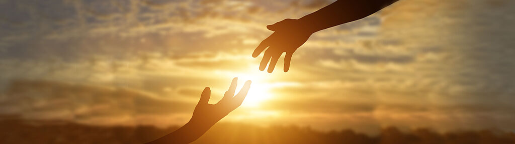 Zwei Hände reichen zu einander und in der Mitte scheint die Sonne. 