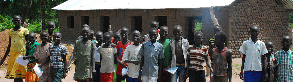 Bildung für den Frieden: Eine grosse, lachende Kinderschar steht vor einem neu gebauten Schulhaus.