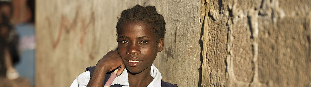 Sambia: Ein Schulmädchen lächelt an eine Wand gelehnt in die Kamera.