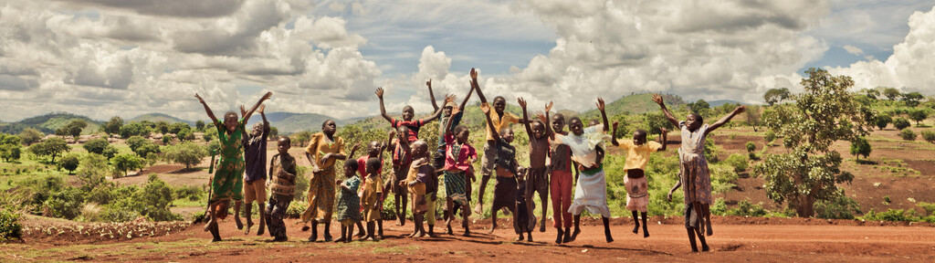 Projektpatenschaften: Eine lachende Kinderschar springt vor einer wunderschönen Landschaft in die Luft und streckt die Hände gegen den Himmel.