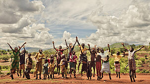 Eine Gruppe afrikanischer Kinder springt in die Luft und streckt die Hände gegen den Himmel