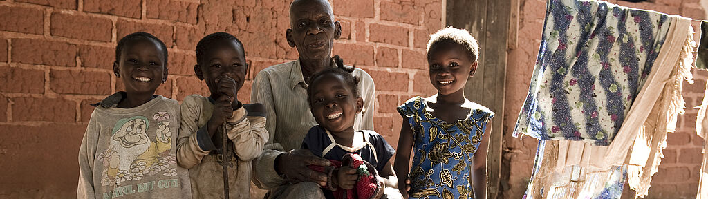 Familie (Grossvater und vier kleine Enkel) aus Sambia sitzt vor ihrem Haus. Bild: Oli Rust, TearFund