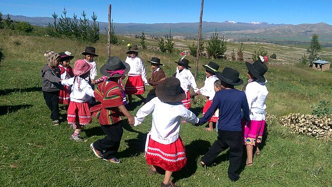 Schulkinder im Hochland Perus halten sich an den Händen und tanzen im Kreis.