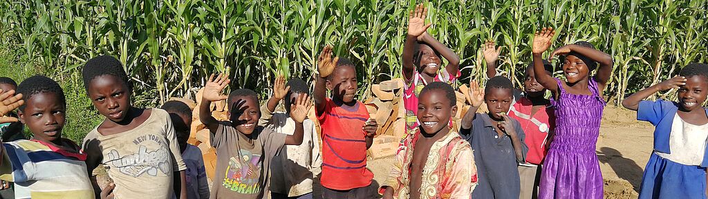 Kinder in Malawi stehen strahlend vor einem Maisfeld.