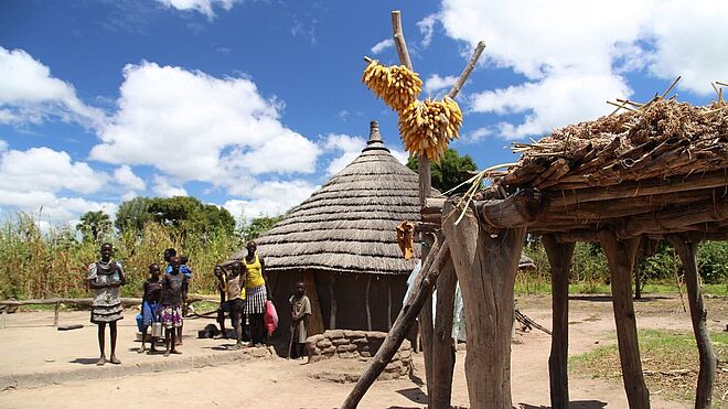 Eine Mutter mit ihren Kindern trocknet Hirse und Mais vor ihrer einfachen Hütte. Bild: Anna Abel / TearFund Schweiz