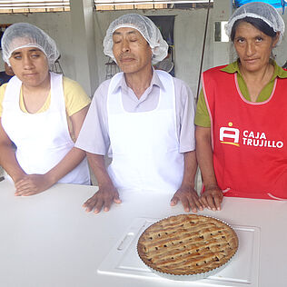 Eine Gruppe von vier BäckerInnen, zwei von ihnen leben mit einer Sehbehinderung, präsentieren einen Kuchen.