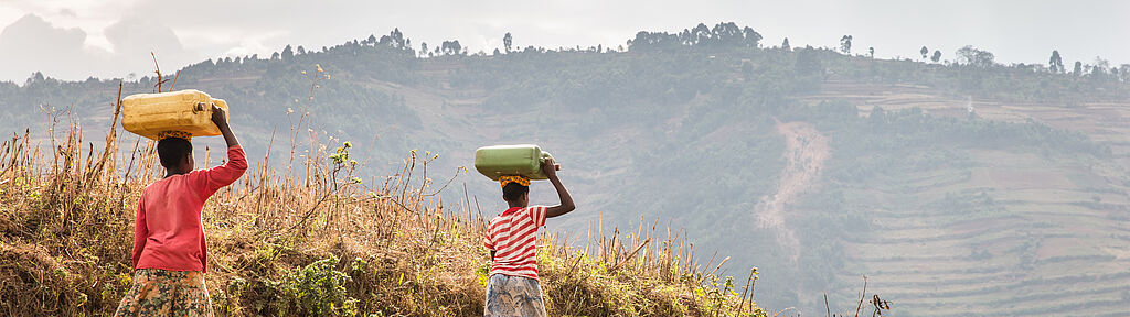 Uganda: Zwei Mädchen laufen mit vollen Wasserkanistern auf dem Kopf einen Hügel hinauf nach Hause.