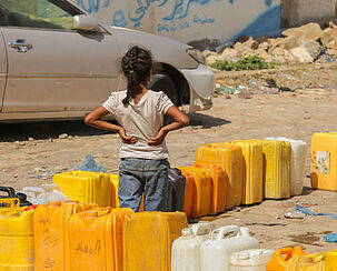 Warten auf kostbares Nass: Ein Mädchen im Jemen steht neben einer Reihe von Wasserkanistern