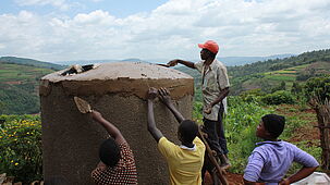 Ugandische Dorfbewohner arbeiten an einem Regenwassertank.